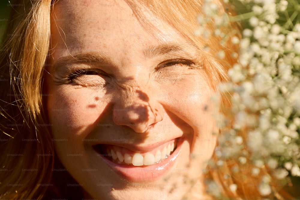 a close up of a person smiling with flowers in the background