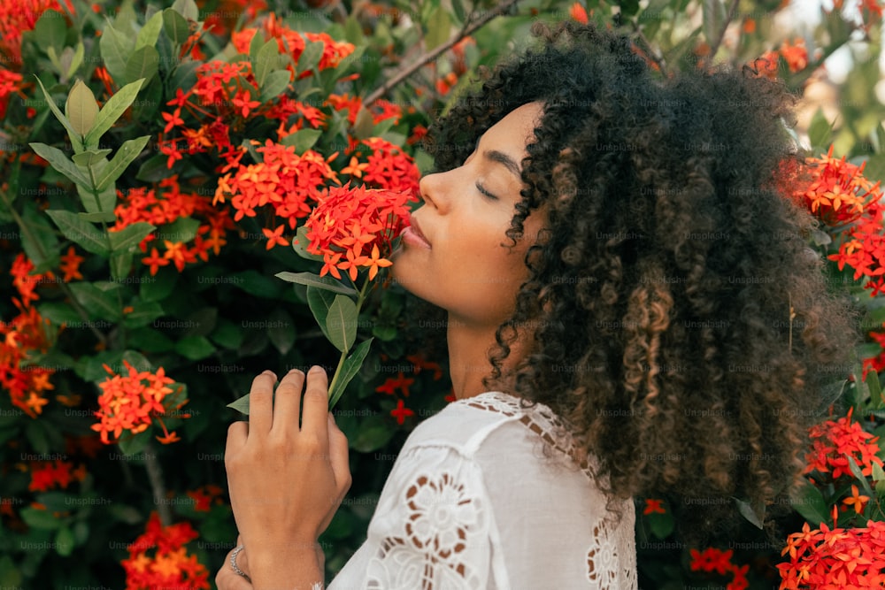 une femme debout devant un buisson de fleurs rouges