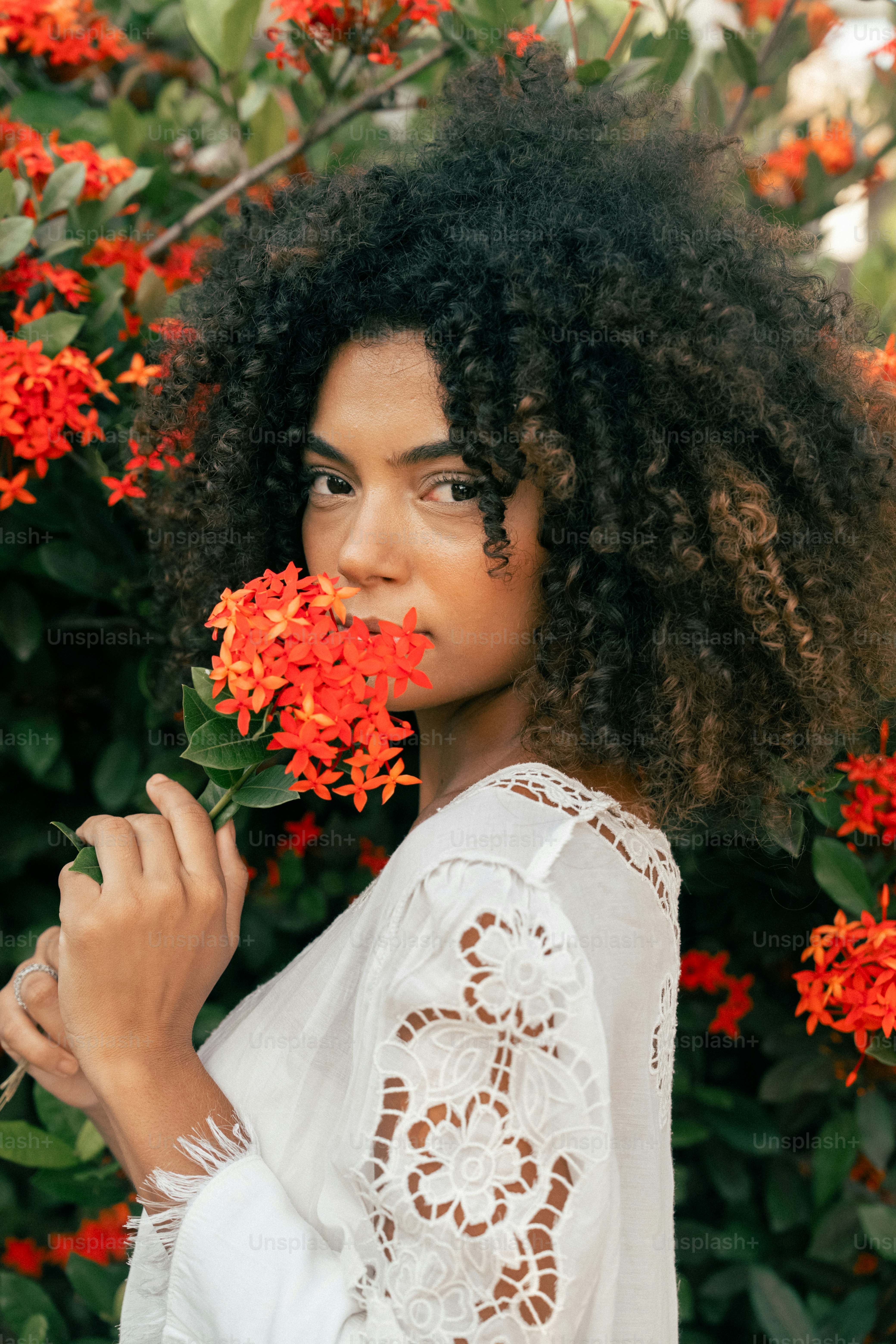 a woman standing in front of a bush with red flowers