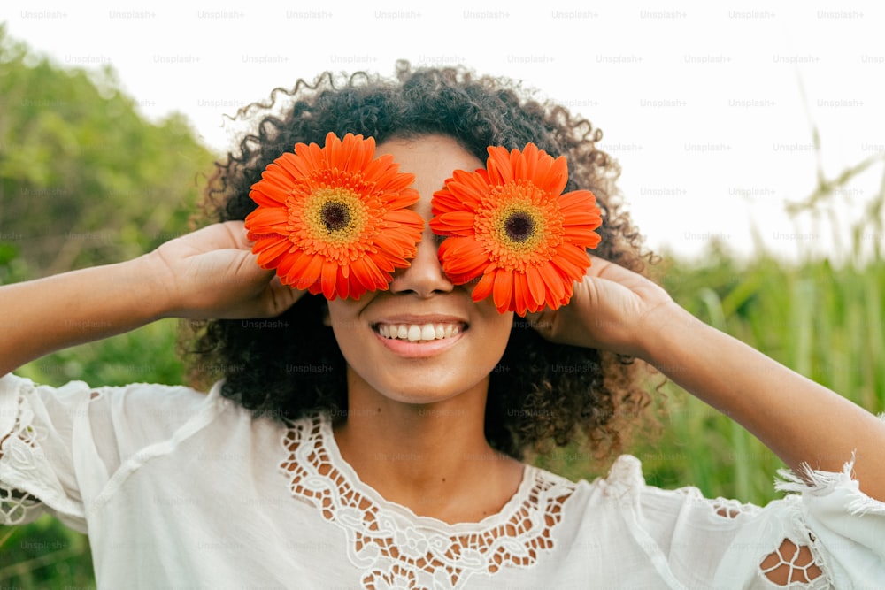 una mujer sosteniendo dos flores naranjas sobre sus ojos