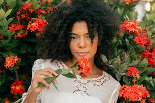 una mujer sosteniendo una flor frente a un arbusto