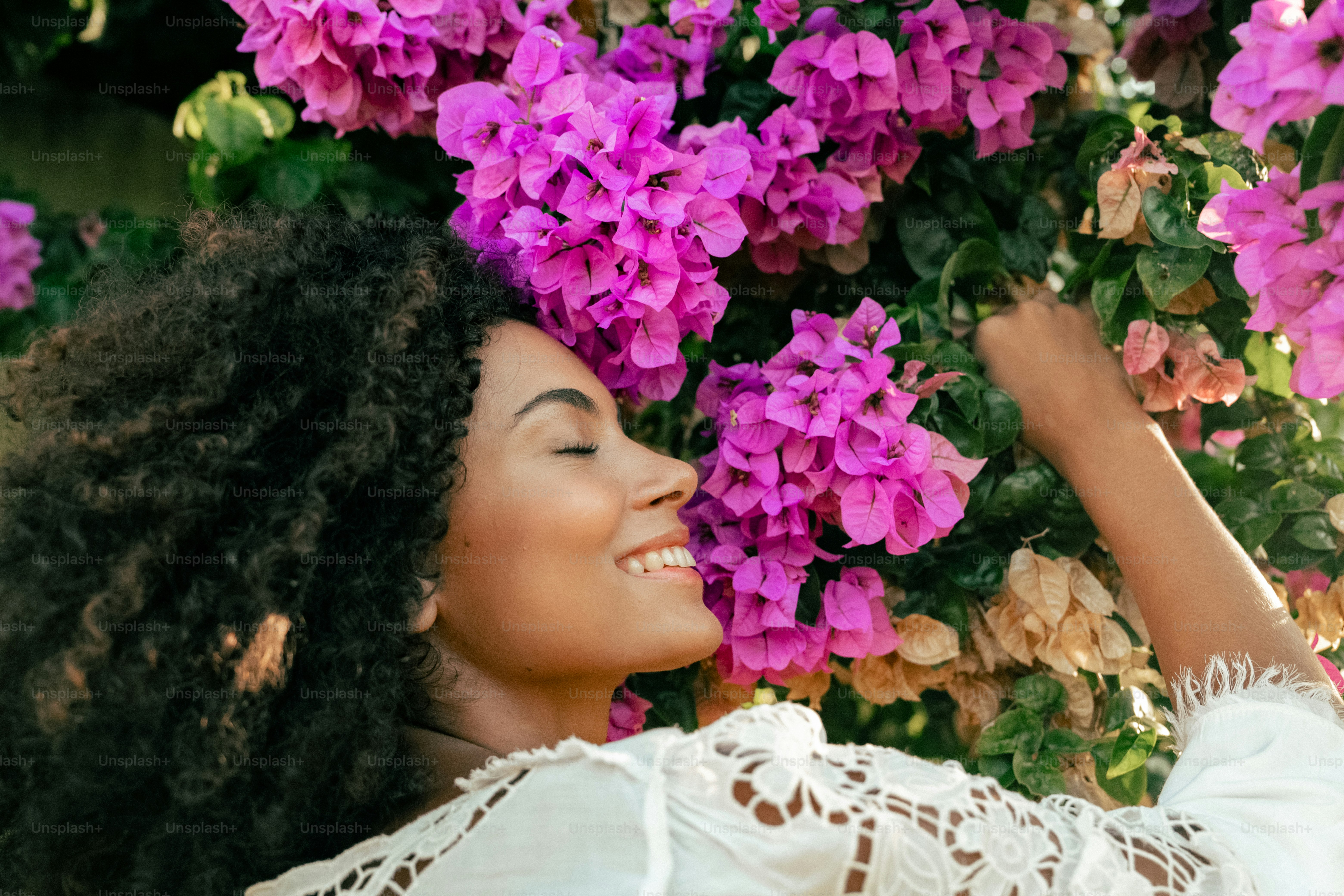 a woman in a white top is smelling a bunch of purple flowers