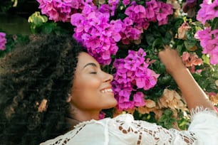 a woman in a white top is smelling a bunch of purple flowers