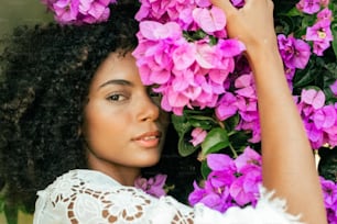 a woman with curly hair standing in front of purple flowers