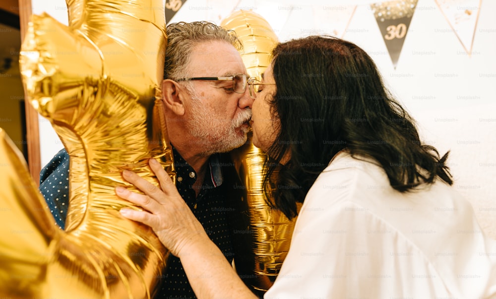 un uomo e una donna che si baciano davanti a palloncini d'oro