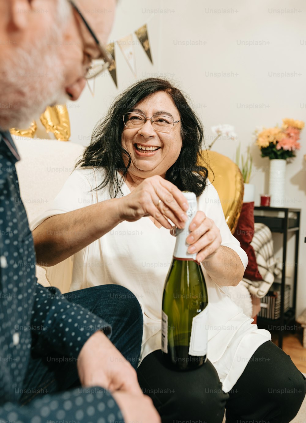 a woman opening a bottle of wine while a man looks on