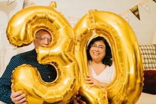 a man and a woman holding up large golden balloons