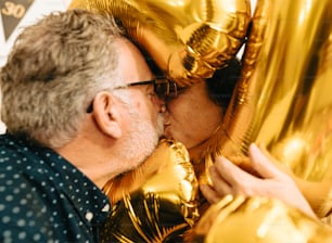 a man kissing a woman in front of gold balloons
