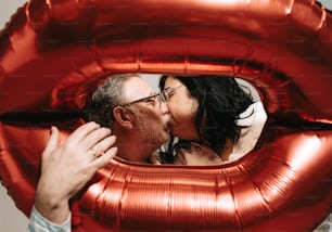 a man kissing a woman through a red balloon