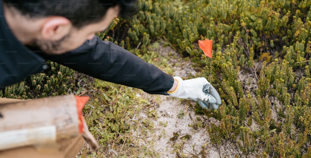 a man in a black jacket and white gloves picking up a plant