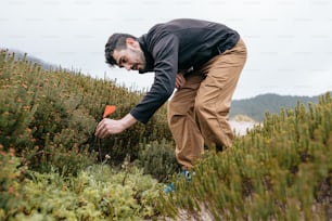 a man in a black shirt and khaki pants picking plants