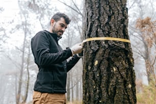 un homme mesurant un arbre avec un ruban à mesurer