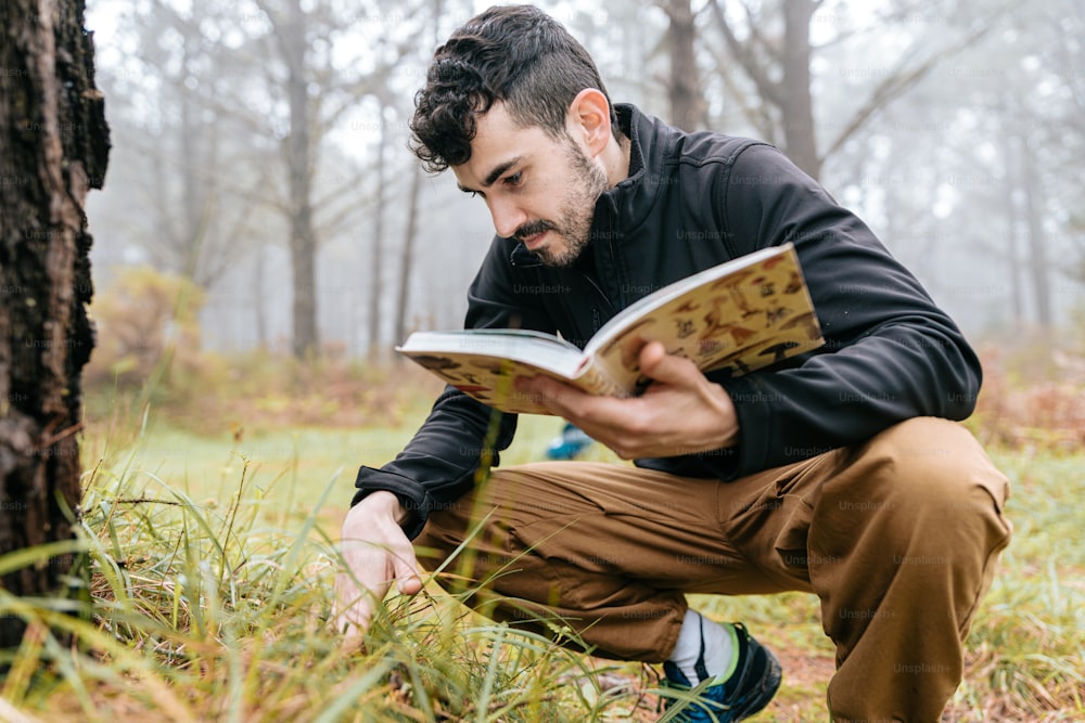 a man kneeling down reading a book in the woods