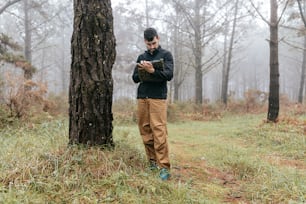 a man standing next to a tree in a forest