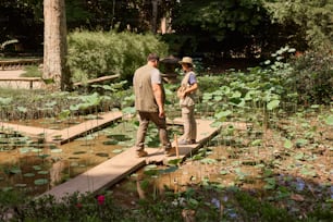 a man and a woman walking across a bridge over a pond