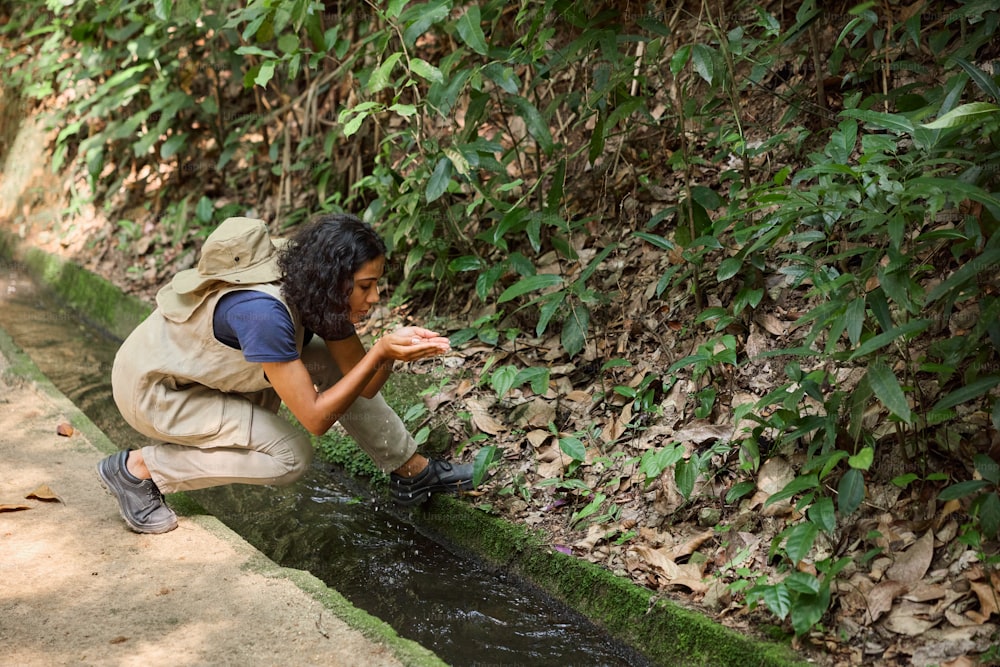 a woman kneeling down next to a small stream