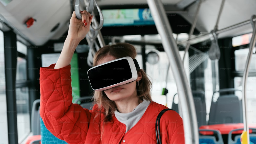 a woman in a red jacket is using a virtual reality device on a bus