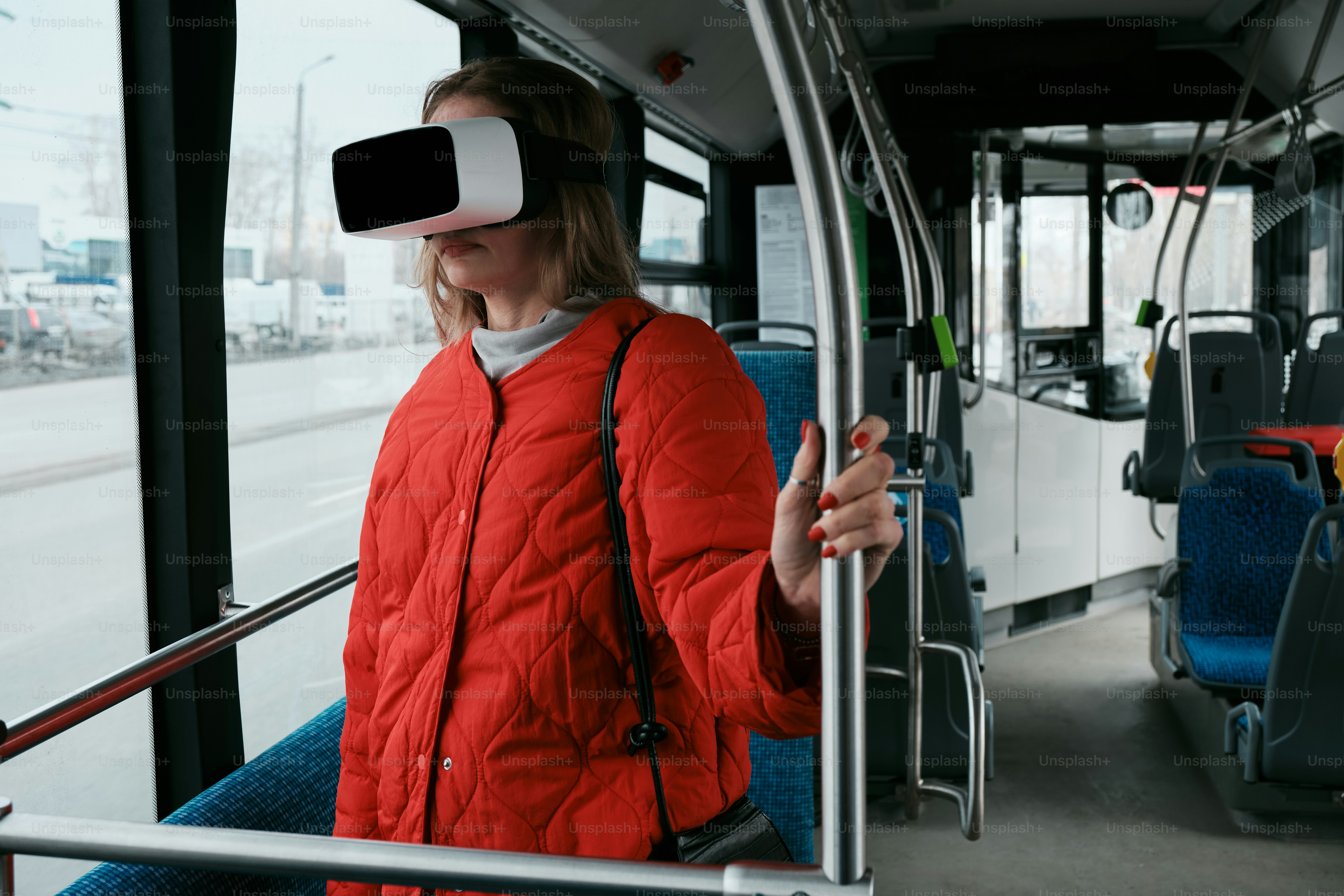 a woman in a red jacket is using a virtual reality device on a bus