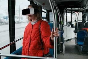 a woman in a red jacket is using a virtual reality device on a bus