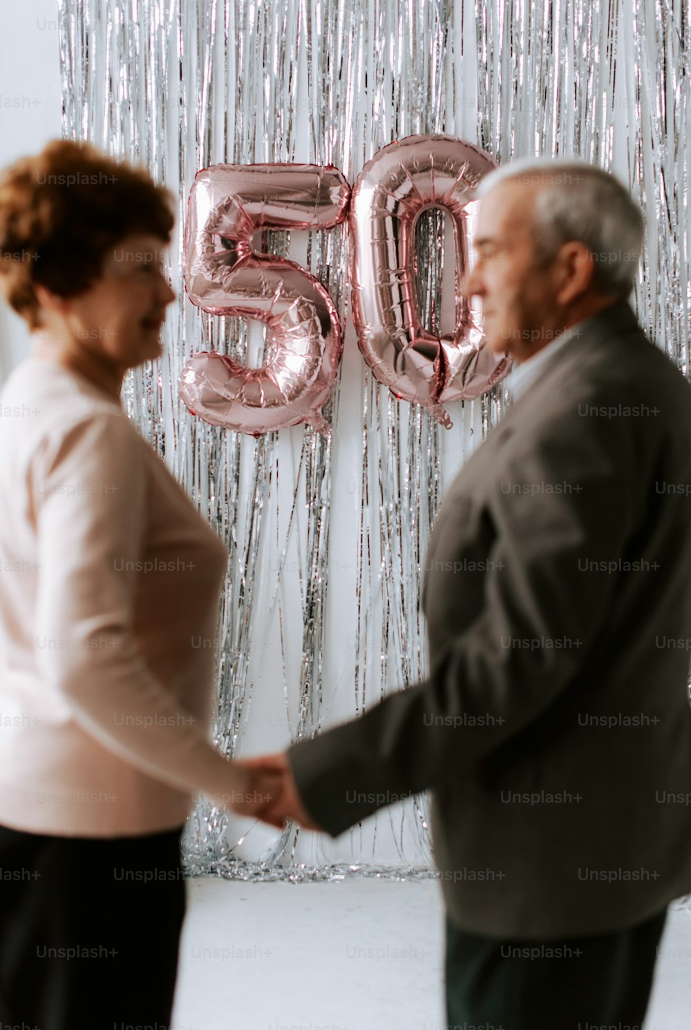 Un hombre y una mujer dándose la mano frente a un gran globo que dice 50