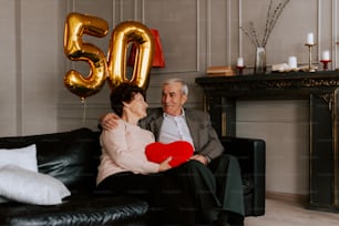 a man and woman sitting on a couch with a heart shaped pillow