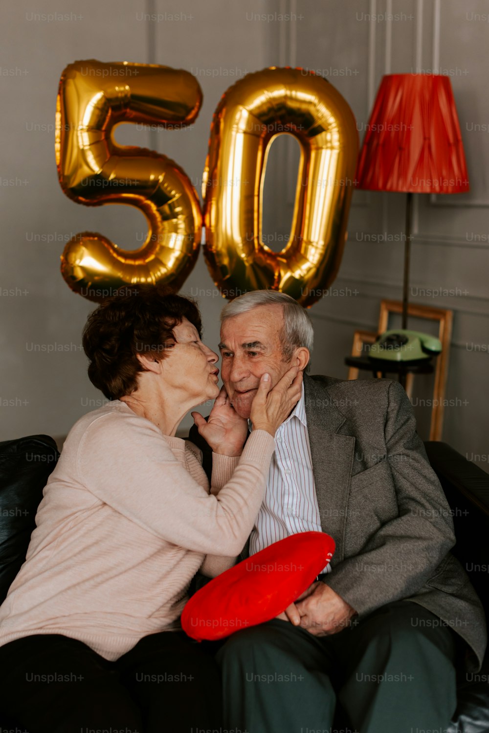 a man and woman sitting on a couch next to a number 50 balloon