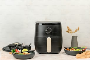 a black air fryer sitting on top of a counter next to bowls of food
