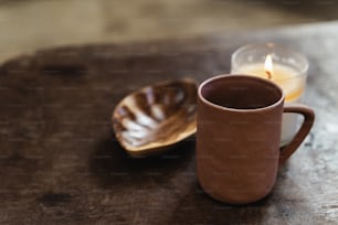 uma xícara de café ao lado de uma vela em uma mesa