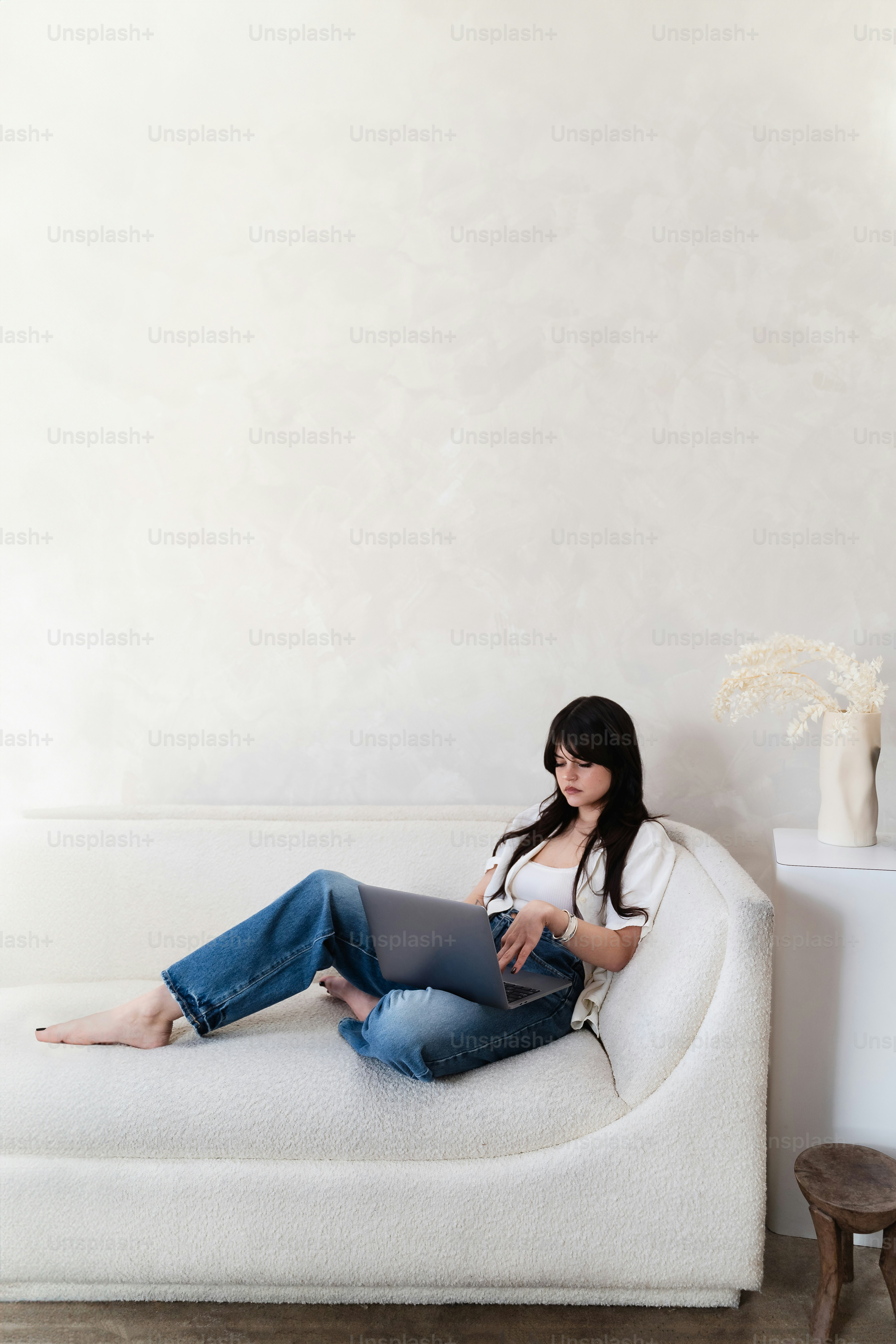 Dark haired woman works from home on a big, fluffy, white couch.