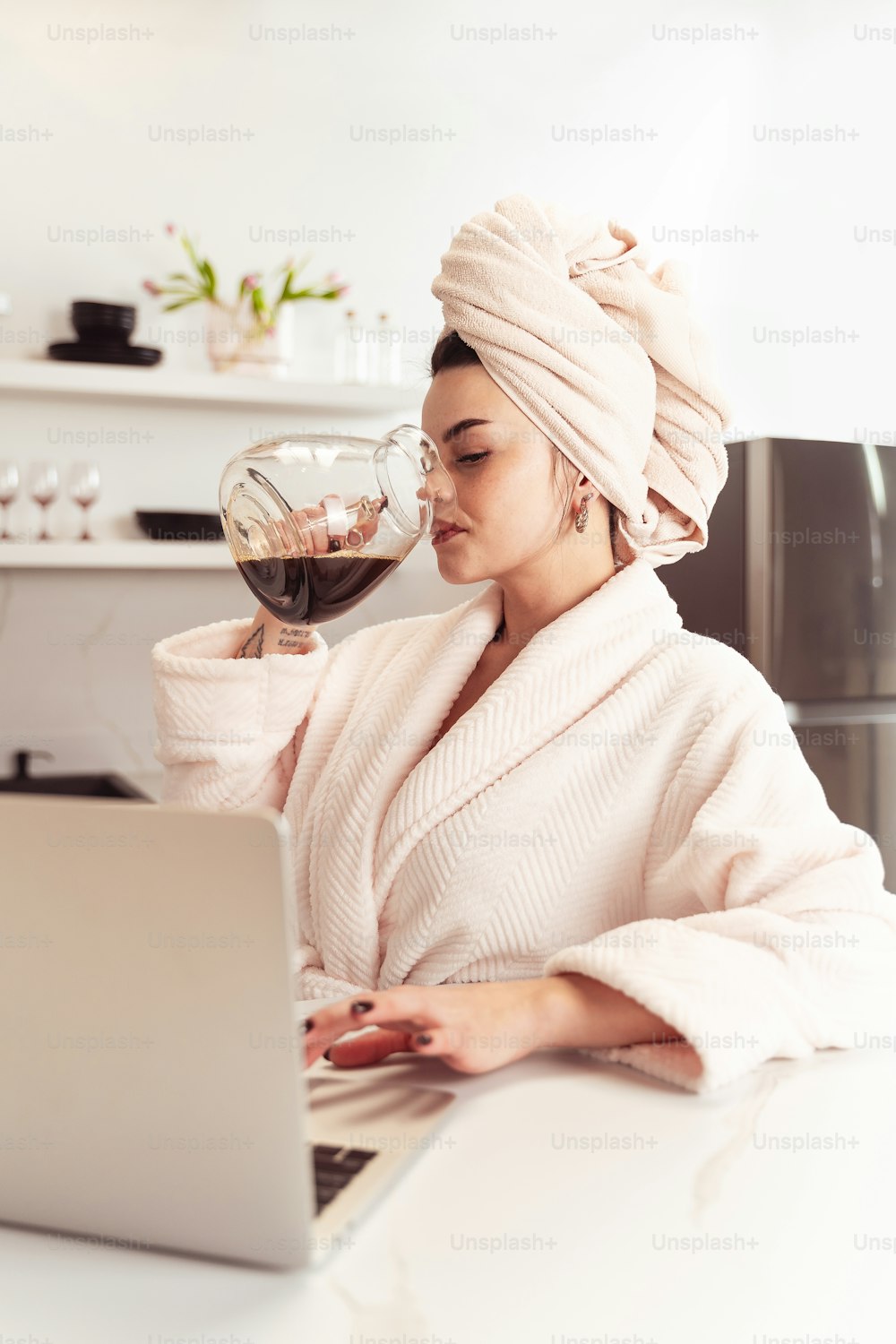 a woman in a bathrobe drinking a glass of wine while using a laptop