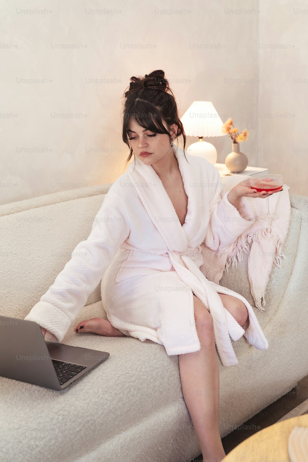 una mujer en bata de baño sentada en un sofá con una computadora portátil