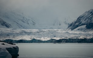 a mountain range covered in snow next to a body of water