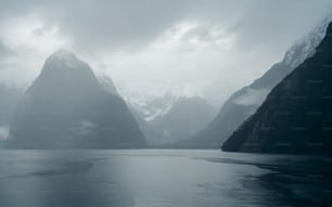 a body of water surrounded by mountains under a cloudy sky