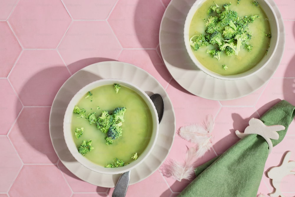 two bowls of broccoli soup on a pink table
