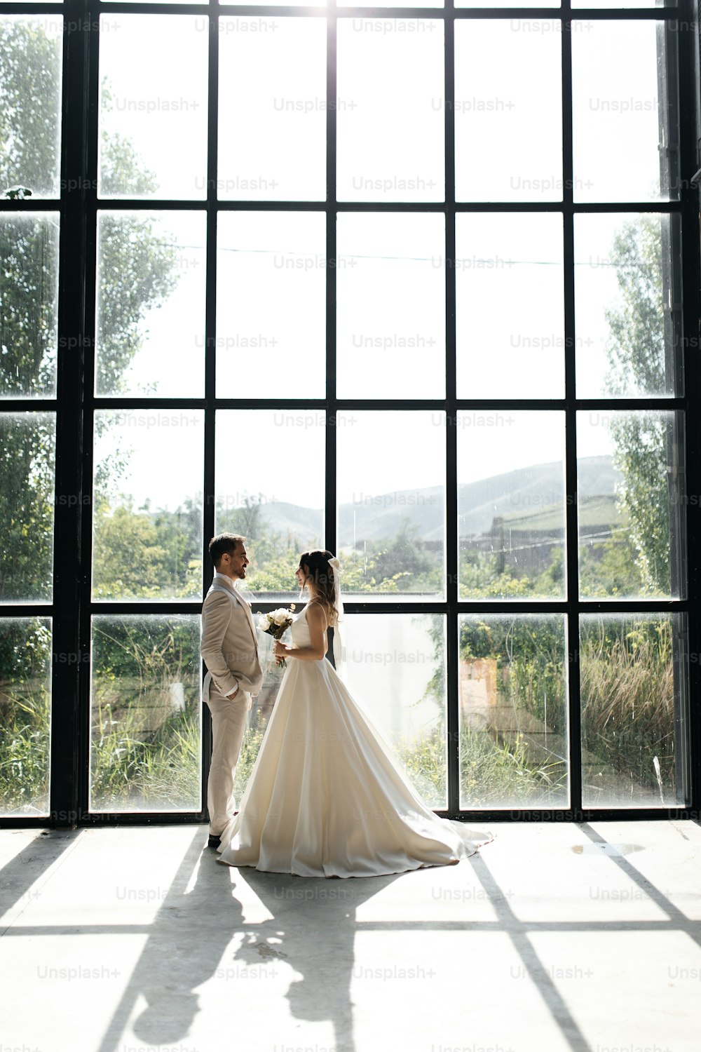 une mariée et un marié debout devant une grande fenêtre