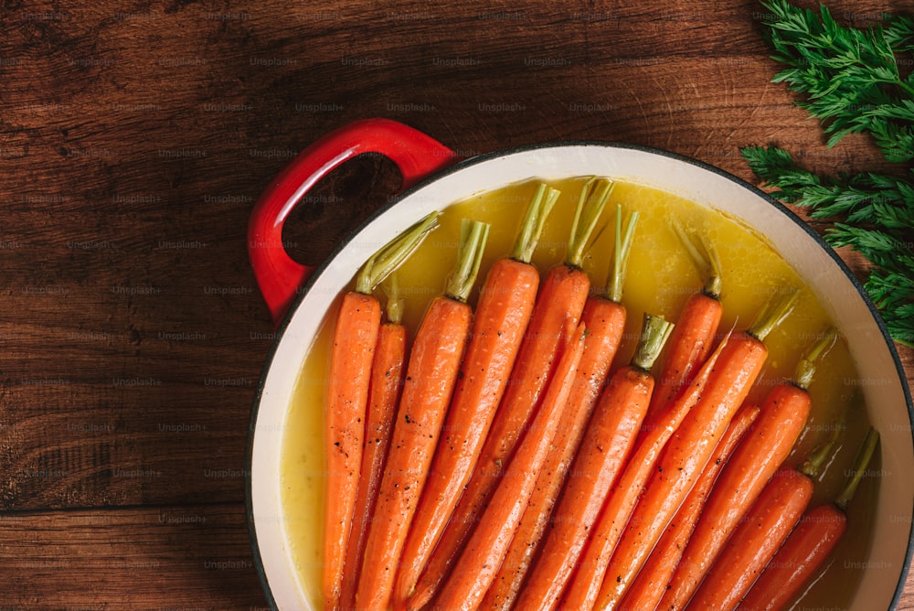 une casserole remplie de carottes à côté d’une tasse rouge