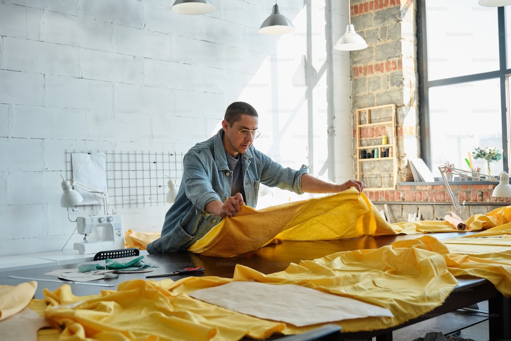 a man sitting on a table working on a piece of cloth