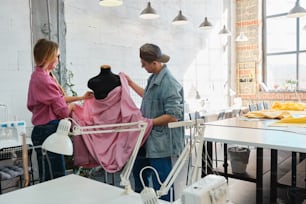 a man and a woman working on a dress on a mannequin