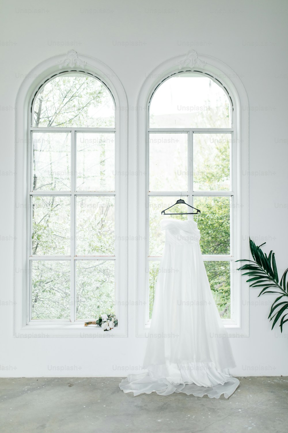 a wedding dress hanging in front of two windows