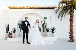 a bride and groom holding hands in front of a cactus arch
