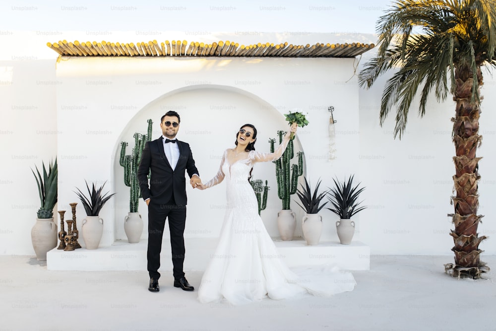 una sposa e uno sposo che si tengono per mano davanti a un arco di cactus