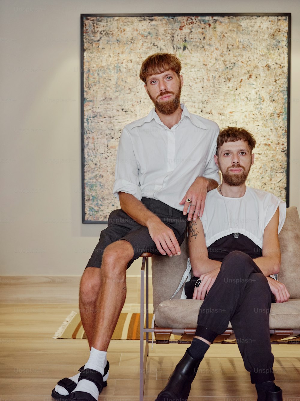 two men sitting on a chair in front of a painting