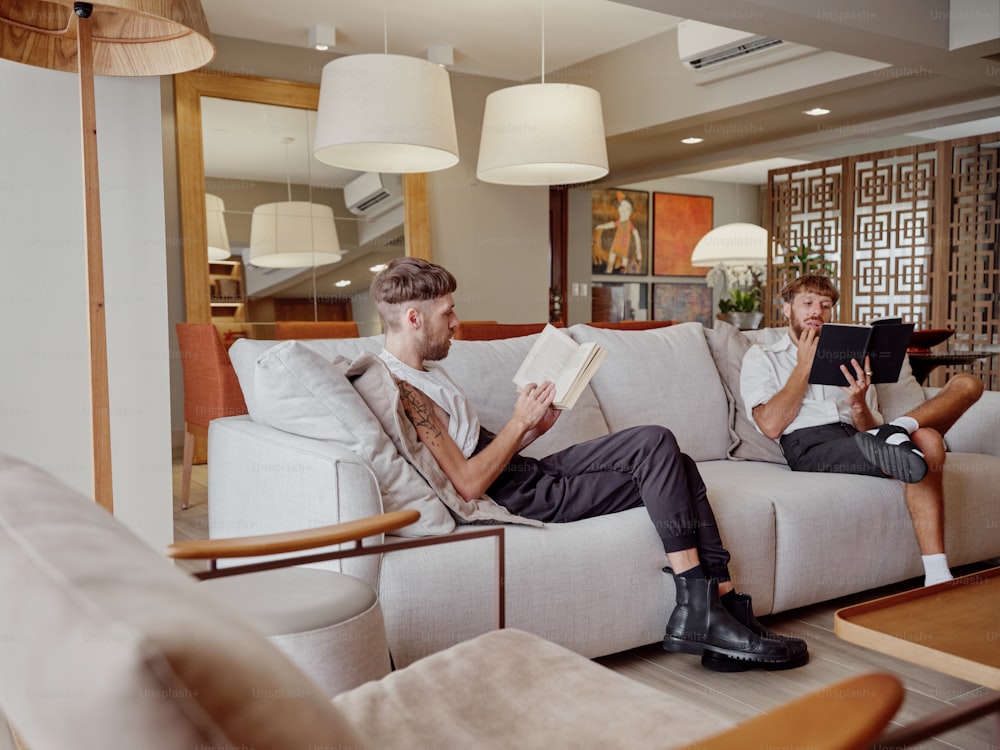 two men sitting on a couch reading a book