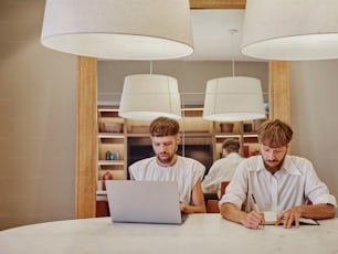 two men sitting at a table working on a laptop