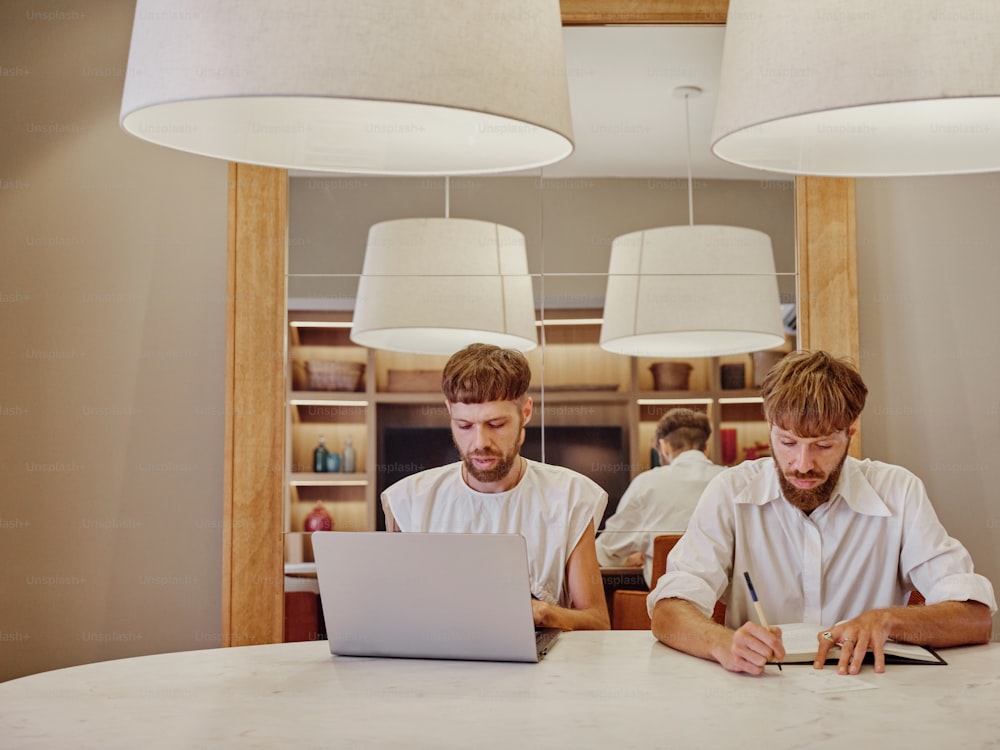 zwei Männer sitzen an einem Tisch und arbeiten an einem Laptop