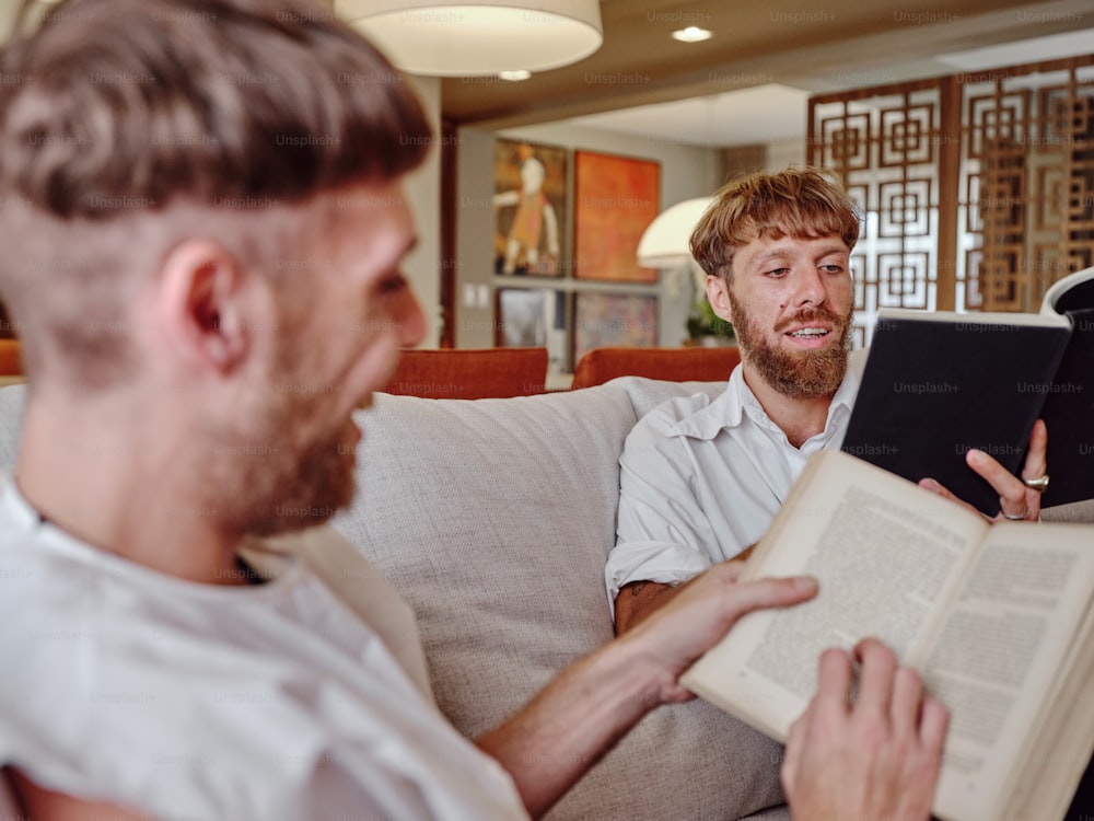 two men sitting on a couch looking at a book
