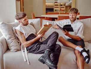 two men sitting on a couch reading books