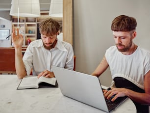 two men sitting at a table working on a laptop