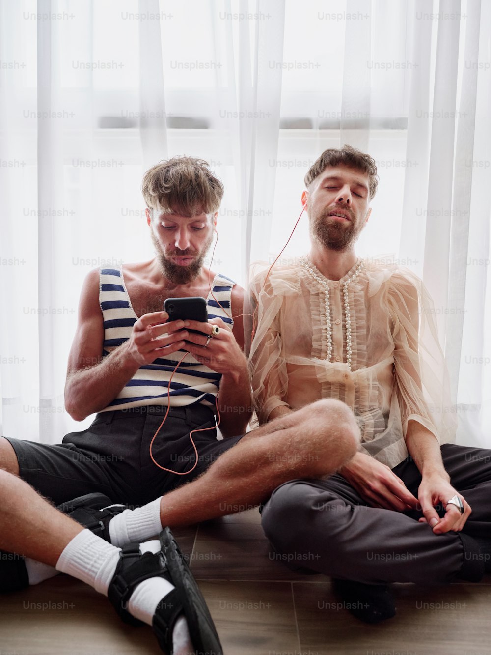 two men sitting on the floor looking at a cell phone