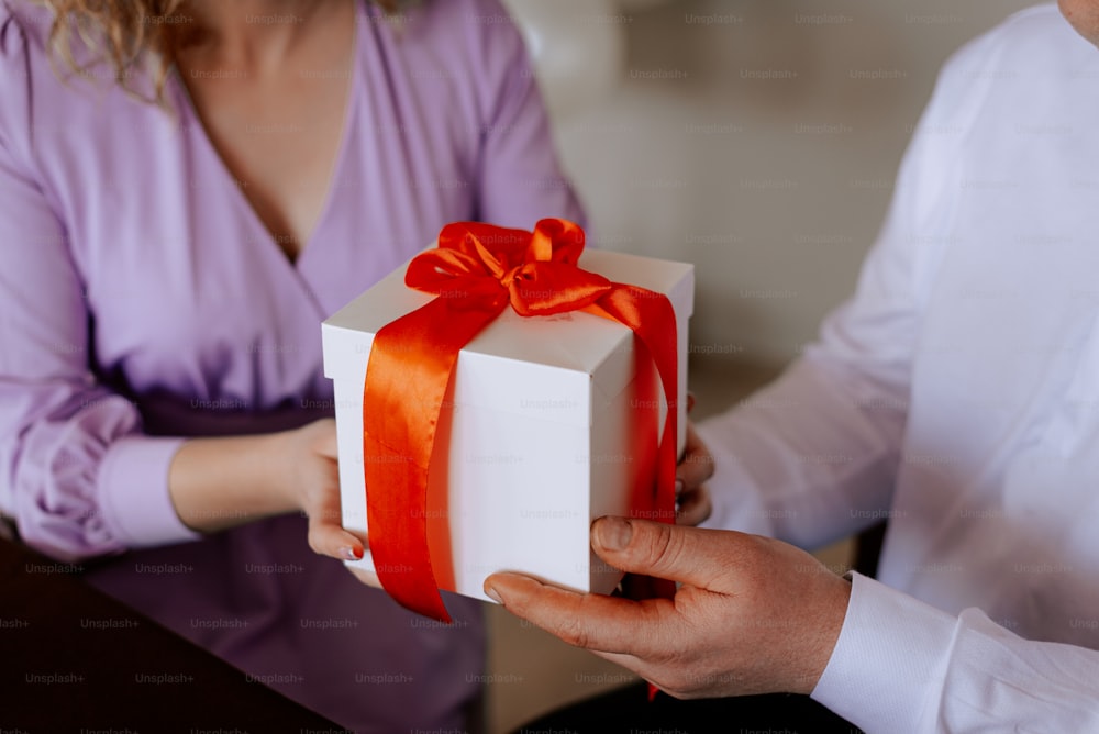 a person holding a white gift box with a red ribbon